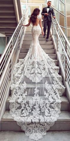 a bride and groom walking down the stairs in their wedding gowns with lace on them