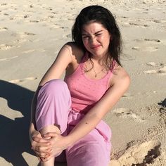 a woman sitting on the beach with her legs crossed and looking at the camera,