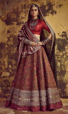 a woman in a red and gold lehenga standing next to an old wall