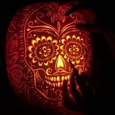 a person carving a pumpkin into the shape of a skull with intricate designs on it