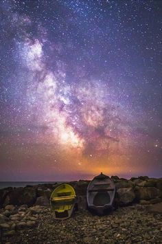 two boats sitting on top of a rocky beach under a night sky