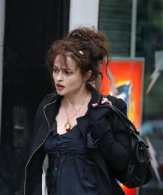 a woman walking down the street with a handbag on her shoulder and wearing a black jacket