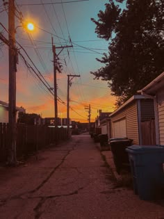 the sun is setting over an alley way with trash cans and garbage cans on either side