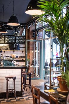 the inside of a restaurant with tables and stools, potted plants on the counter