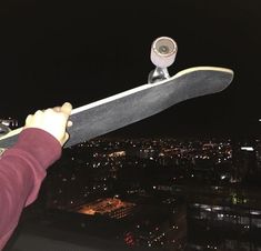 a person holding a skateboard in front of a cityscape at night time