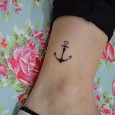 a small anchor tattoo on the side of a woman's leg, with roses around it