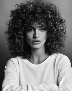 a black and white photo of a woman with long curly hair wearing a sweater looking at the camera