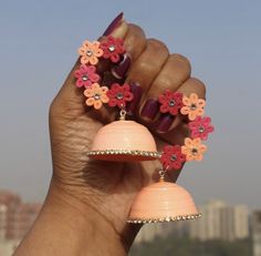 a hand holding two pink and orange flower shaped earrings on it's ear rings