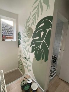 some paint cans are sitting on the floor in front of a wall with leaves painted on it