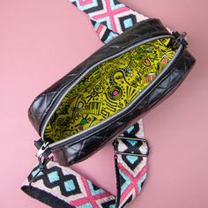 a black and yellow bag on top of a pink background with an interesting pattern around it