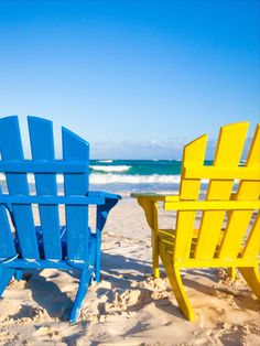 two yellow and blue chairs sitting on top of a sandy beach