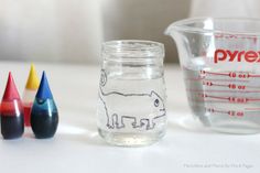 some crayons are next to a glass jar with a drawing on the side