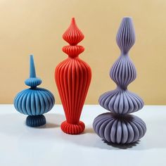 three different colored vases sitting next to each other on a white counter top in front of a beige wall