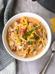 a white bowl filled with chicken and corn soup next to tortilla chips on a gray surface