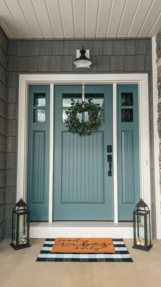 a blue front door with two lanterns and a welcome mat