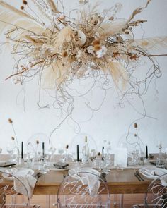 a dining room table is set with clear chairs and an arrangement of dried flowers hanging from the ceiling