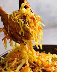 a wooden spoon full of shredded carrots and other food in a black bowl on top of a table