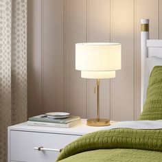 a bed with a green bedspread next to a white night stand and lamp