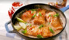 a skillet filled with fish and garnishes on top of a table