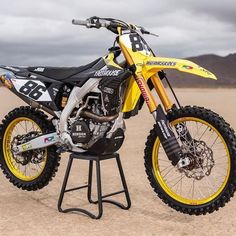 a yellow and black dirt bike parked on top of a metal stand in the desert