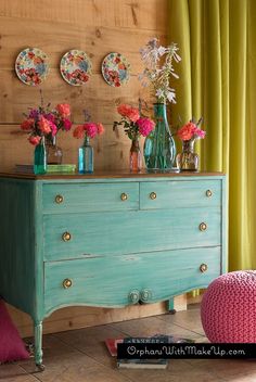 a blue dresser with flowers and plates on it