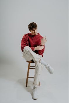 a young man sitting on top of a wooden chair holding his hand up in the air