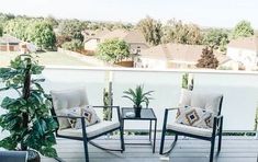 two chairs and a table on a deck with potted plants in the foreground