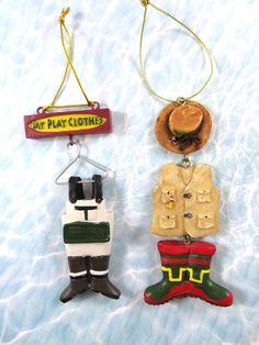 three christmas ornaments are hanging on a string in the snow, one is wearing a hat and another has a sign that says eat play clothes