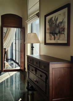 a room with a dresser, lamp and painting on the wall