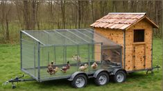 a chicken coop with chickens in it on the grass next to a trailer and trees