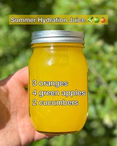 a hand holding a mason jar filled with oranges and green apples, labeled summer hydration juice