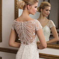 a woman in a white wedding dress looking at herself in the mirror with her back to the camera