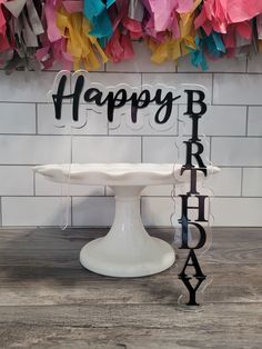 a happy birthday cake on a pedestal with streamers hanging from the wall behind it