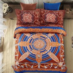 an orange and blue comforter set with decorative designs on the bottom, along with matching pillows