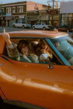 two women in an orange car giving the peace sign