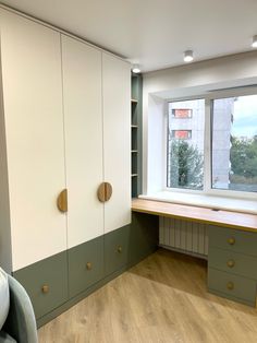 an empty room with green and white cupboards next to a large window in the corner