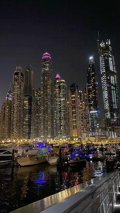 the city skyline is lit up at night, with boats docked in the harbor and skyscrapers