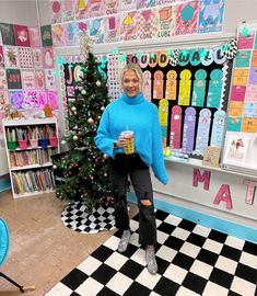 a woman standing in front of a christmas tree holding a drink and smiling at the camera