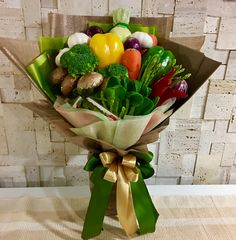 a bouquet of fresh vegetables wrapped in brown paper and tied with gold ribbon on a table