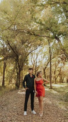 a man and woman standing in the middle of a forest with leaves on the ground