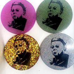 four round stickers with the faces of three famous people on them, all in different colors