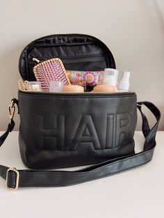 a black bag with hair products in it sitting on a table next to a mirror