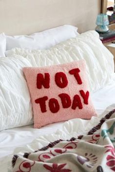 a pillow that says not today on it sitting on a bed with white sheets and pillows