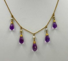 A stunning Victorian - Belle Epoque Amethyst Necklace with 5 gorgeous graduated Briolette Cut Amethysts set in a perfect 14 Karat Yellow Gold Necklace. The Amethysts have the most wonderful purple color and the briolette cut of the gems brings out their vivid beauty. The amethysts are graduated giving the necklace such balance and beauty. The amethysts hang from lovely natural white pearls set in 14 Karat Gold. The necklace is full of the romance and delicate style of the Victorian - Edwardian era. A perfect jewel for everyday or for the most glamorous affair. The gold is the most beautiful antique gold with the warmth and color we all just love. The necklace hangs beautifully around the neck. The design is full of the delicate romance of the age and is so special with the amethysts which 1800s Jewelry, Amethyst Set, Antique Jewelry Necklace, Necklace Antique, Yellow Gold Necklace, Wire Necklace, Edwardian Era, Pearl Set, Amethyst Necklace