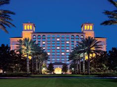 the hotel is lit up at night in front of palm trees and green lawns