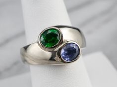 "Absolutely stunning, this bold unisex ring would make a fantastic alternative engagement ring, right-hand ring, or anniversary piece! The ring is simply made, with 18K white gold forming the shanks, and classic bezel set heads holding the stones. Two stunning gemstones are featured in this piece, a sapphire featuring its benchmark quality cornflower blue hue, and the other a deep Kelly green tsavorite garnet, wonderfully cut and set securely in its sleek bezel! Metal: 18K White Gold Gem: Sapphi Tsavorite Garnet Ring, Aquamarine Cocktail Ring, Two Stone Ring, Alternative Engagement Ring, Demantoid Garnet, Tsavorite Garnet, Bypass Ring, Right Hand Rings, Hand Ring