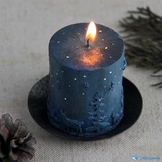 a lit candle sitting on top of a black plate next to pine cones and needles