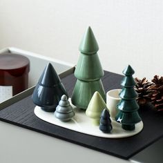 small ceramic christmas trees sitting on top of a tray next to a pinecone