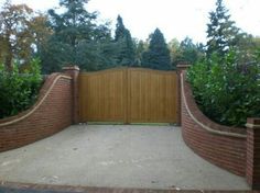 a brick fence with a wooden gate in the middle and trees around it on either side