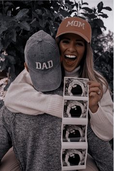 a woman holding onto a man's hat while he holds up his dad's photo